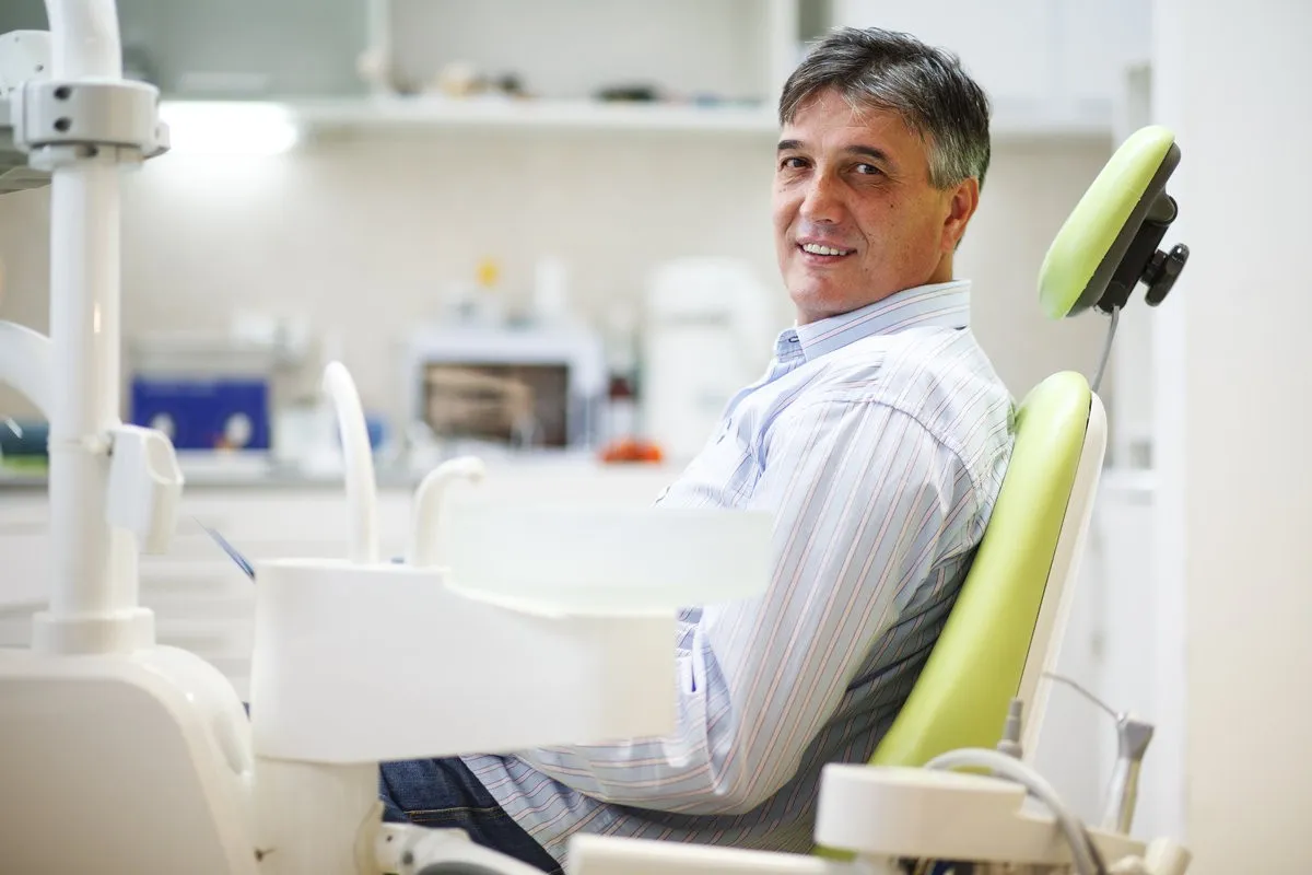 Man pointing at bright smile - Sunrise Dental Arts Care Senior male patient on dental chair waiting for the treatment.