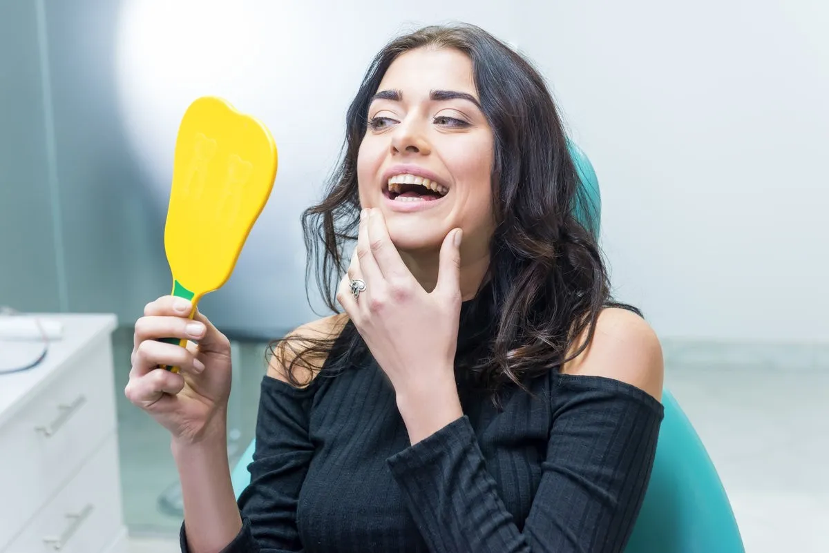 Couple smiling while looking at phone - Sunrise Dental Arts Care Lady looking at her teeth. Woman holding mirror, dentist office.