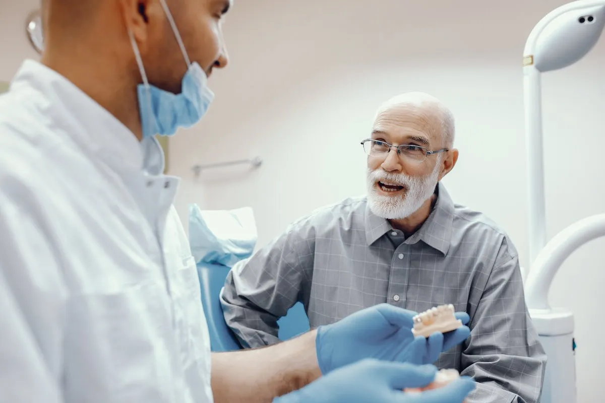 Man pointing at bright smile - Sunrise Dental Arts Care Dentist explaining old man about dentures