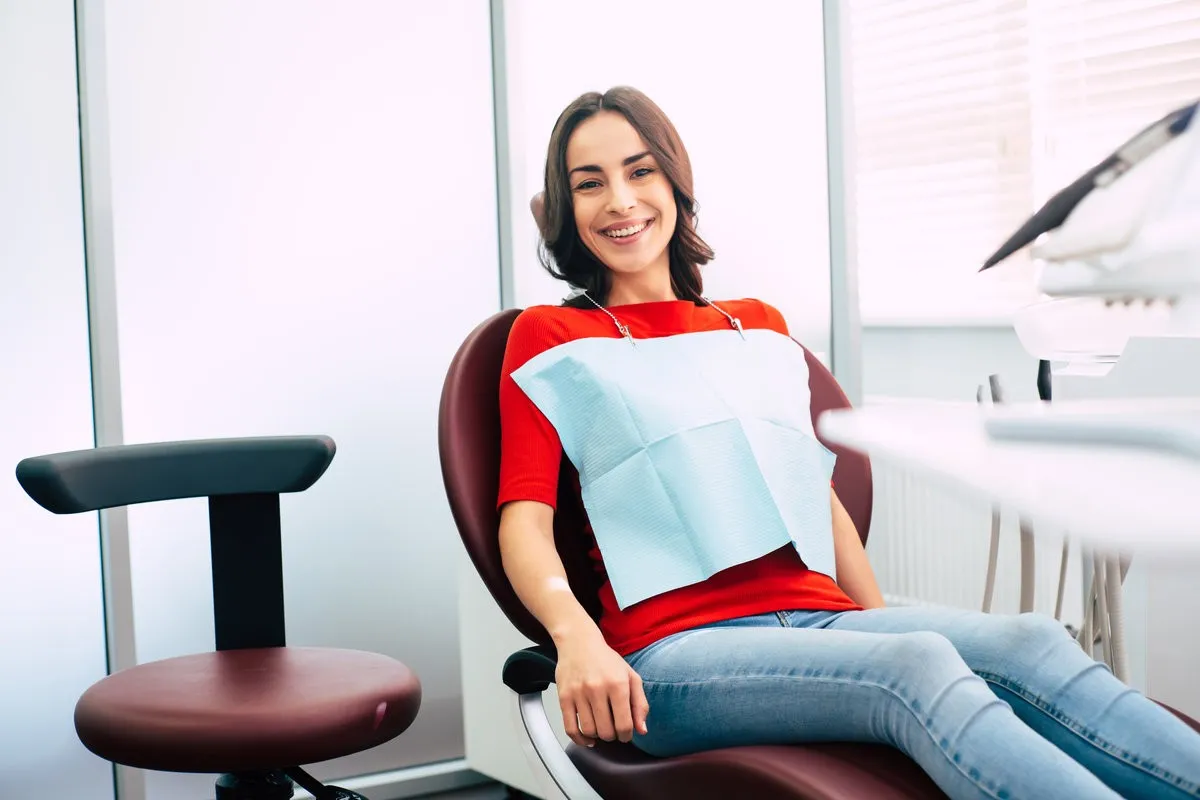 Couple smiling while looking at phone - Sunrise Dental Arts Care Ready to roll. Thin cute girl clothed in red sweater and denim jeans is sitting in the dental chair and waiting for the doctor with all of the pleasant emotions.