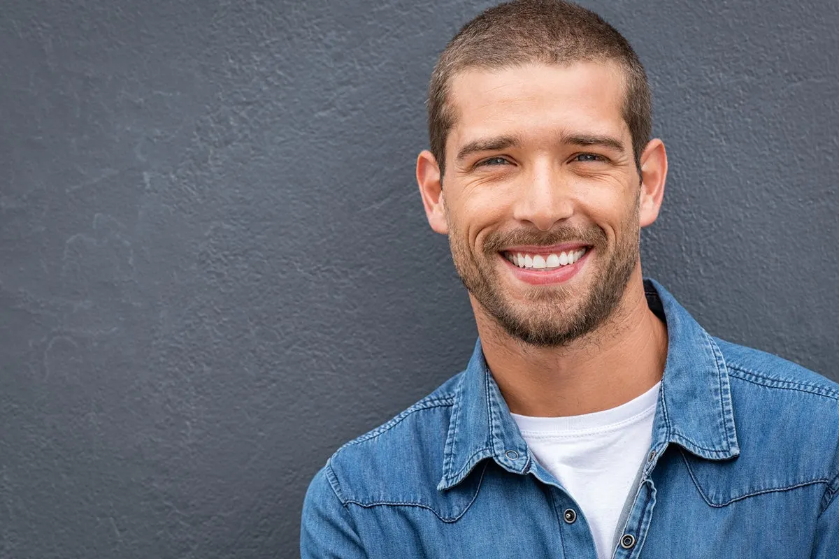 Closeup portrait of a happy young man smiling on gray background. Handsome casual guy with beard looking at camera. Portrait of a cheerful stylish man isolated against gray wall with copy space.