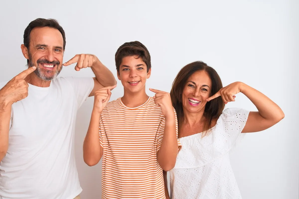 Couple smiling while looking at phone - Sunrise Dental Arts Care Happy family pointing their beautiful teeth