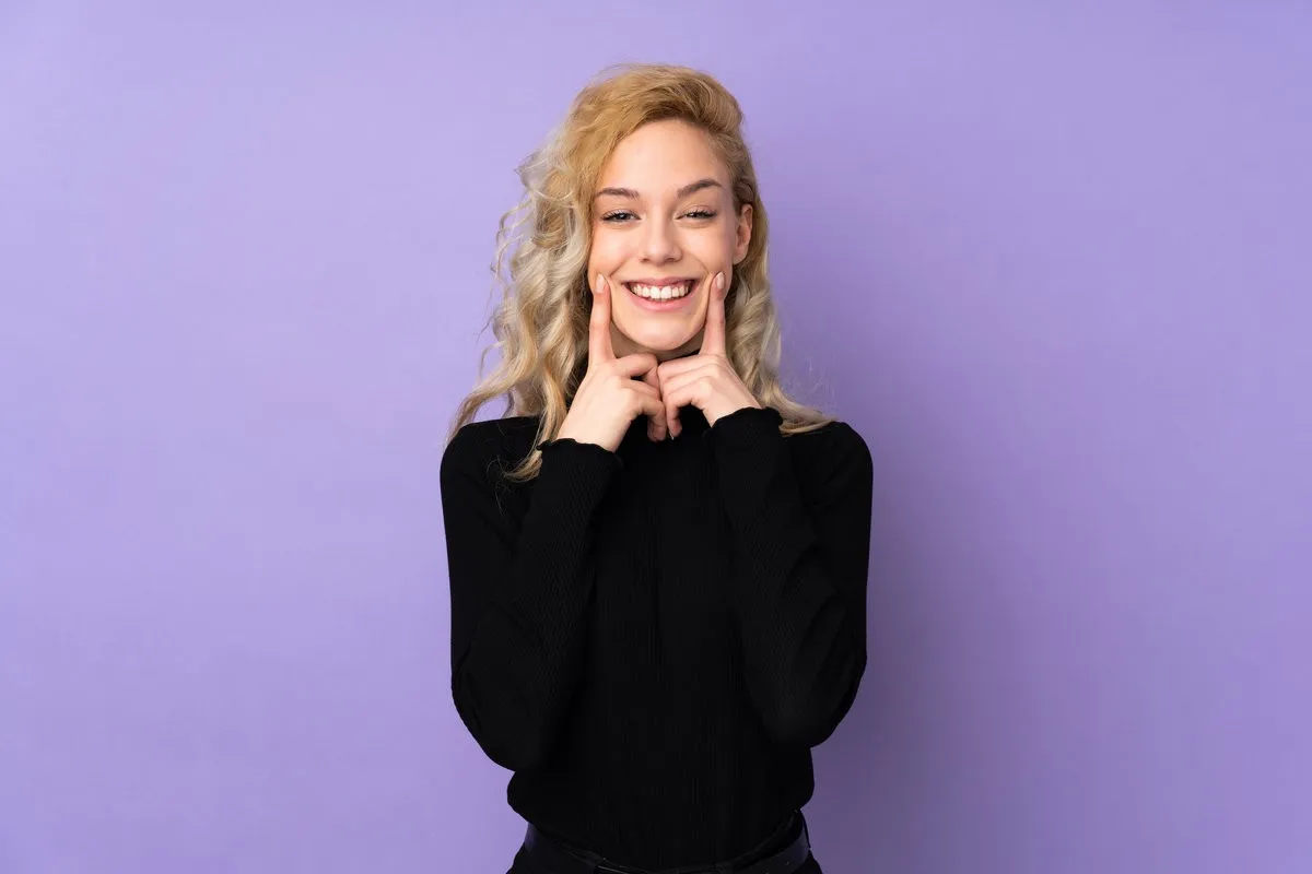 Happy couple smiling outdoors - Sunrise Dental Arts Care Young blonde woman isolated on purple background smiling with a happy and pleasant expression