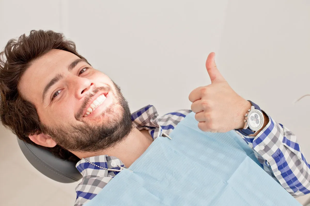Man pointing at bright smile - Sunrise Dental Arts Care young man and woman in a dental examination at dentist