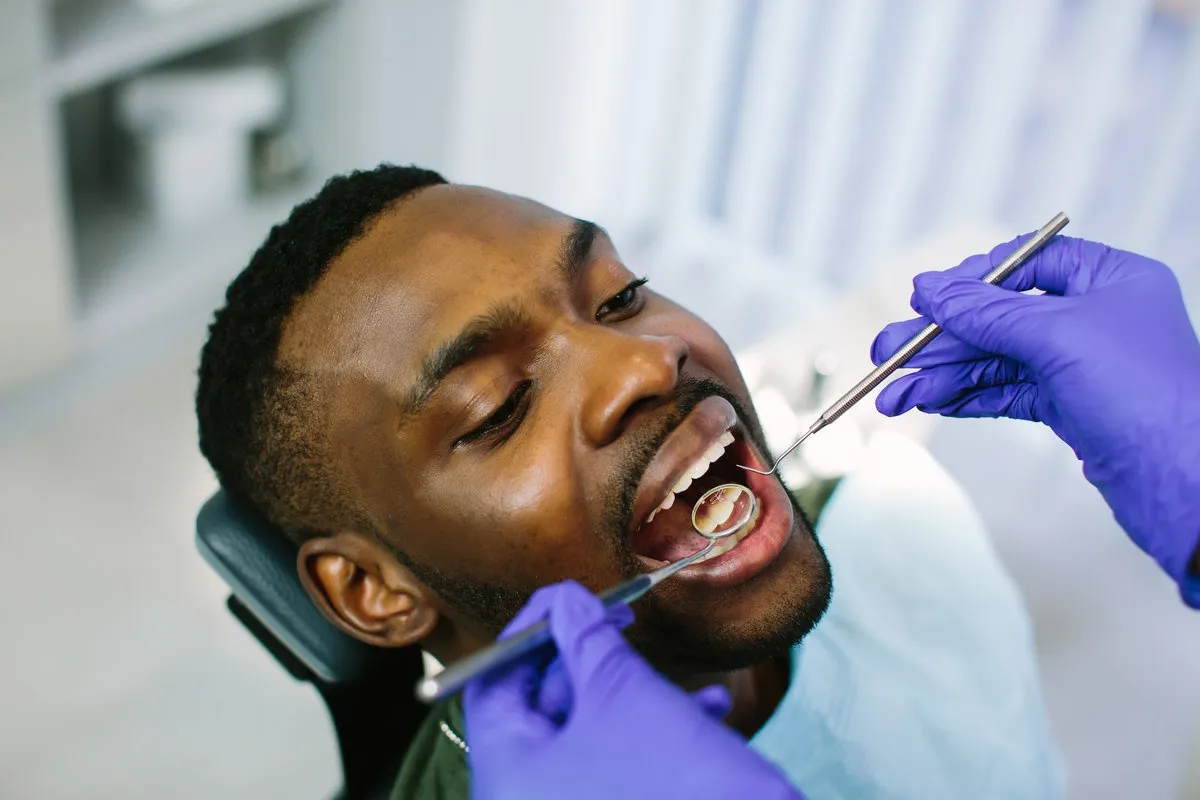 Man pointing at bright smile - Sunrise Dental Arts Care African male patient getting dental treatment in dental clinic