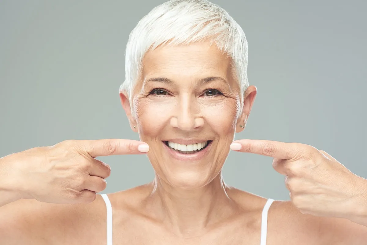 Couple smiling while looking at phone - Sunrise Dental Arts Care Beautiful Caucasian smiling senior woman with short grey hair pointing at her teeth and looking at camera. Beauty photography.