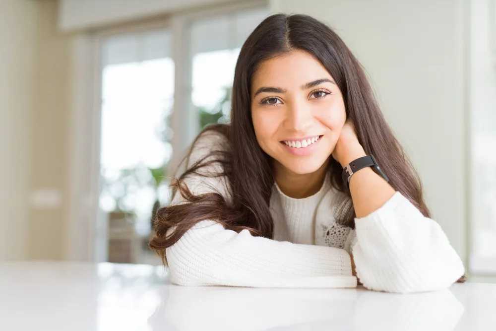 Young woman smiling indoors - Mission Hills Dentist A cheerful young woman with long dark hair smiling warmly while sitting indoors, showcasing her bright and healthy teeth - Mission Hills Dentist.