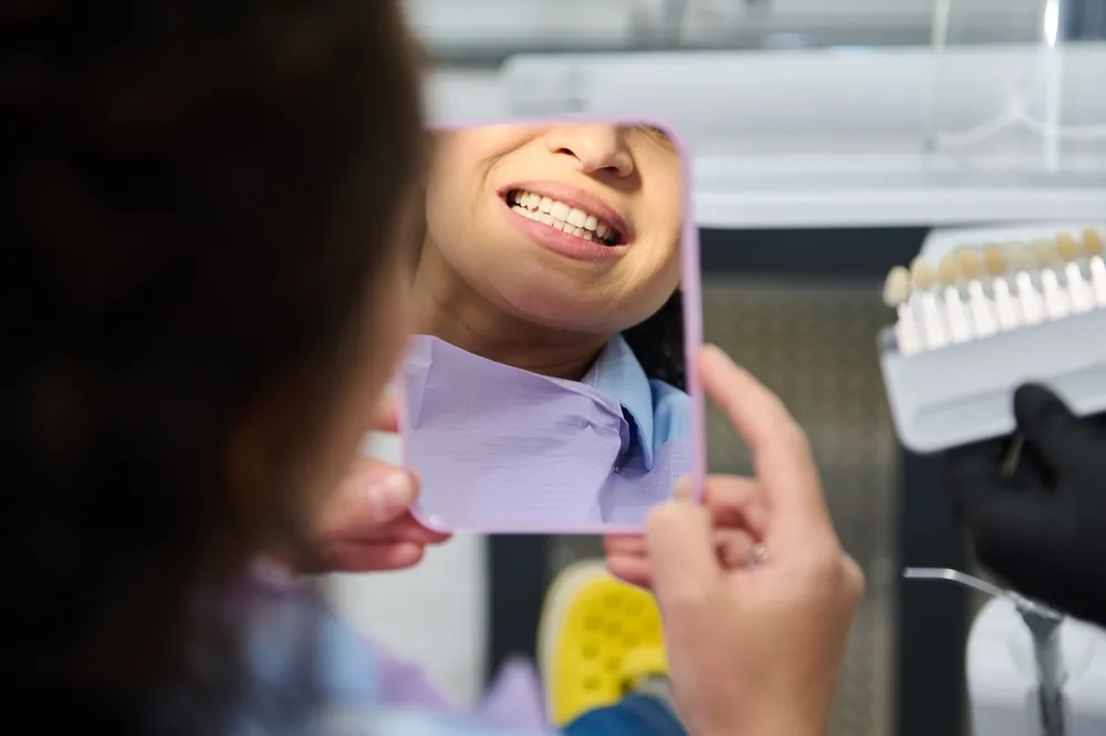 Female patient admiring her new smile in a mirror after veneer placement