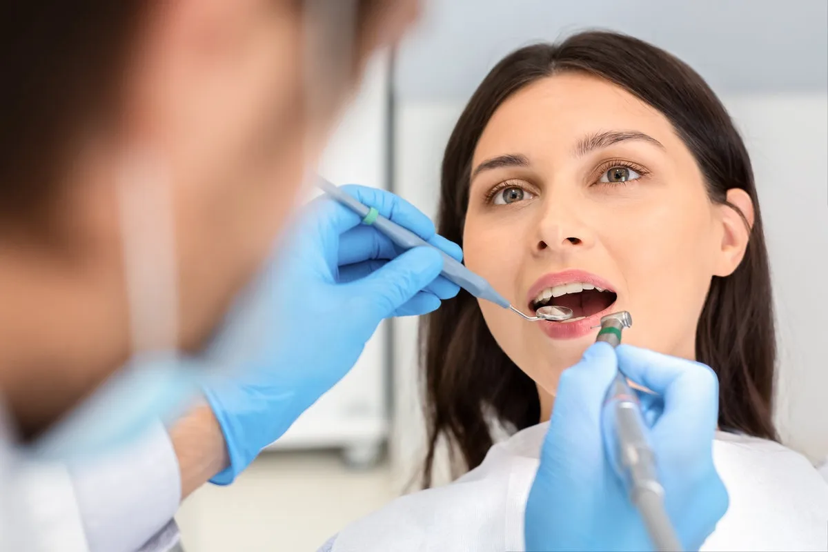 Man pointing at bright smile - Sunrise Dental Arts Care Close up of female patient during treatment at dentist