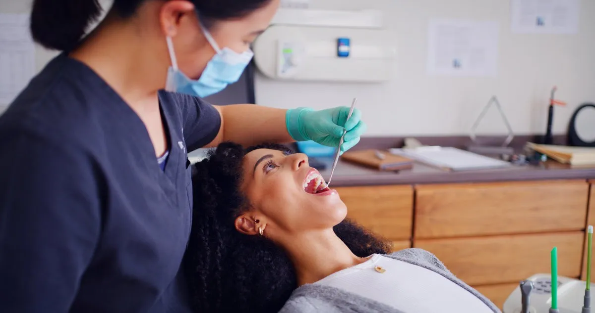 Man pointing at bright smile - Sunrise Dental Arts Care Dentist, patient and inspection with mouth mirror for teeth assessment, oral exam and appointment in office. Dental care, specialist and women with tools for cavity check, gum health and consultation