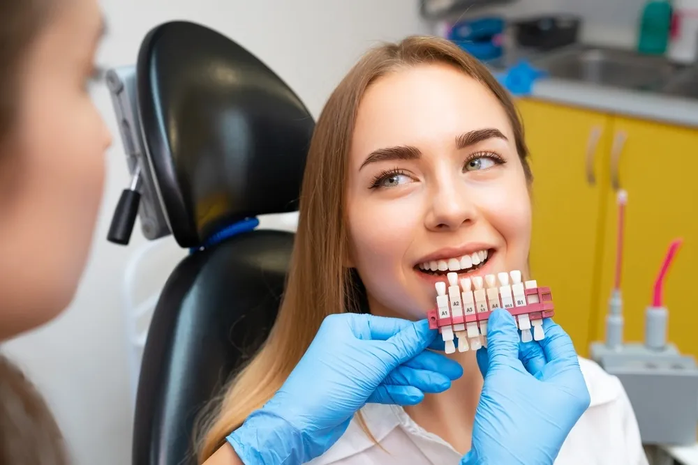 Dentist selects a shade of teeth whitening using shade guide to young patient with perfect smile - Porcelain Veneers in Hillcrest