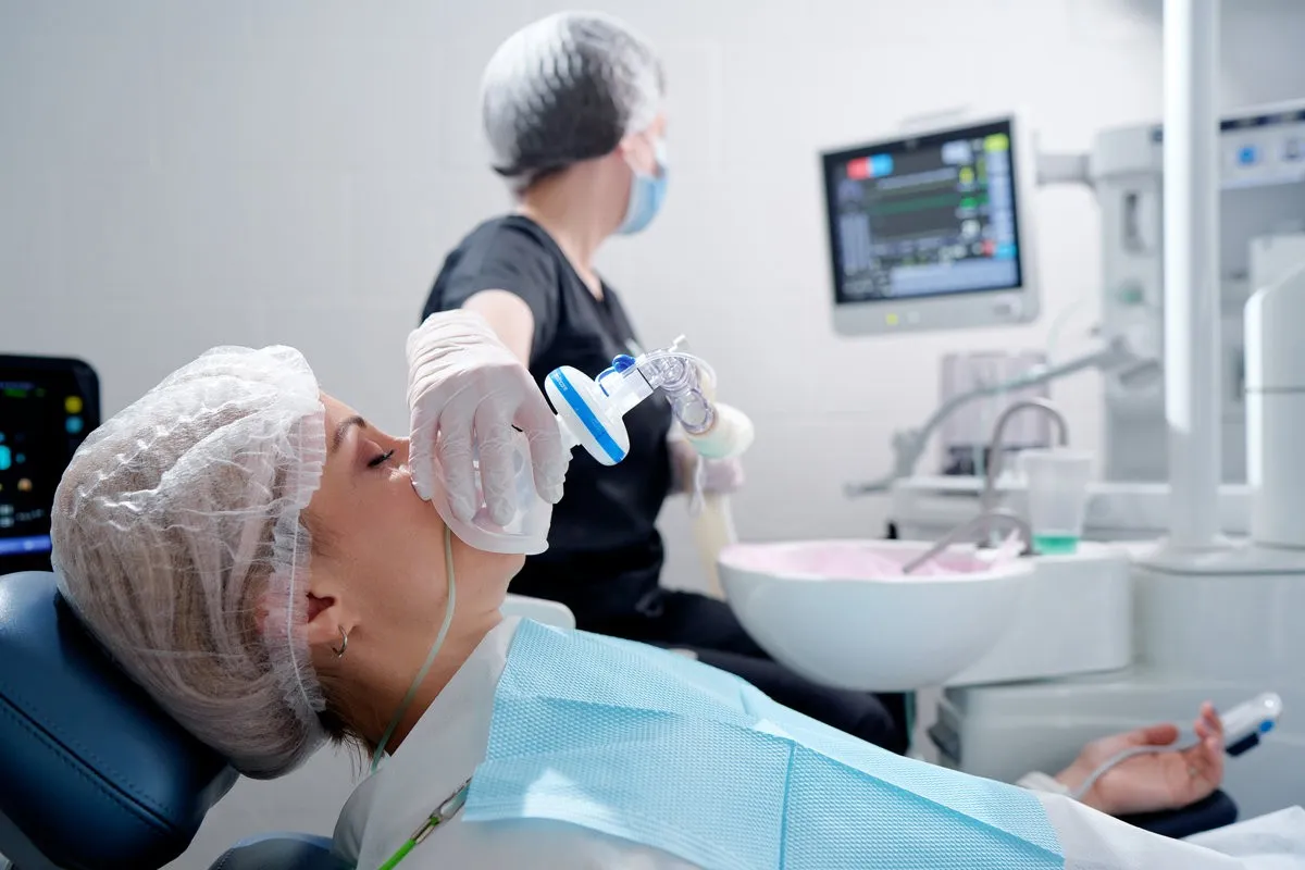 Man pointing at bright smile - Sunrise Dental Arts Care Doctor making anesthesia while female patient lying in dentist chair