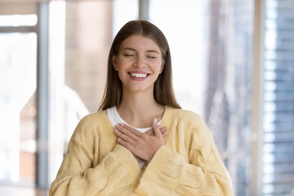 Woman smiling with gratitude - Mission Hills Dentist A young woman smiling with hands over her chest, radiating confidence and positivity with her healthy teeth - Mission Hills Dentist.