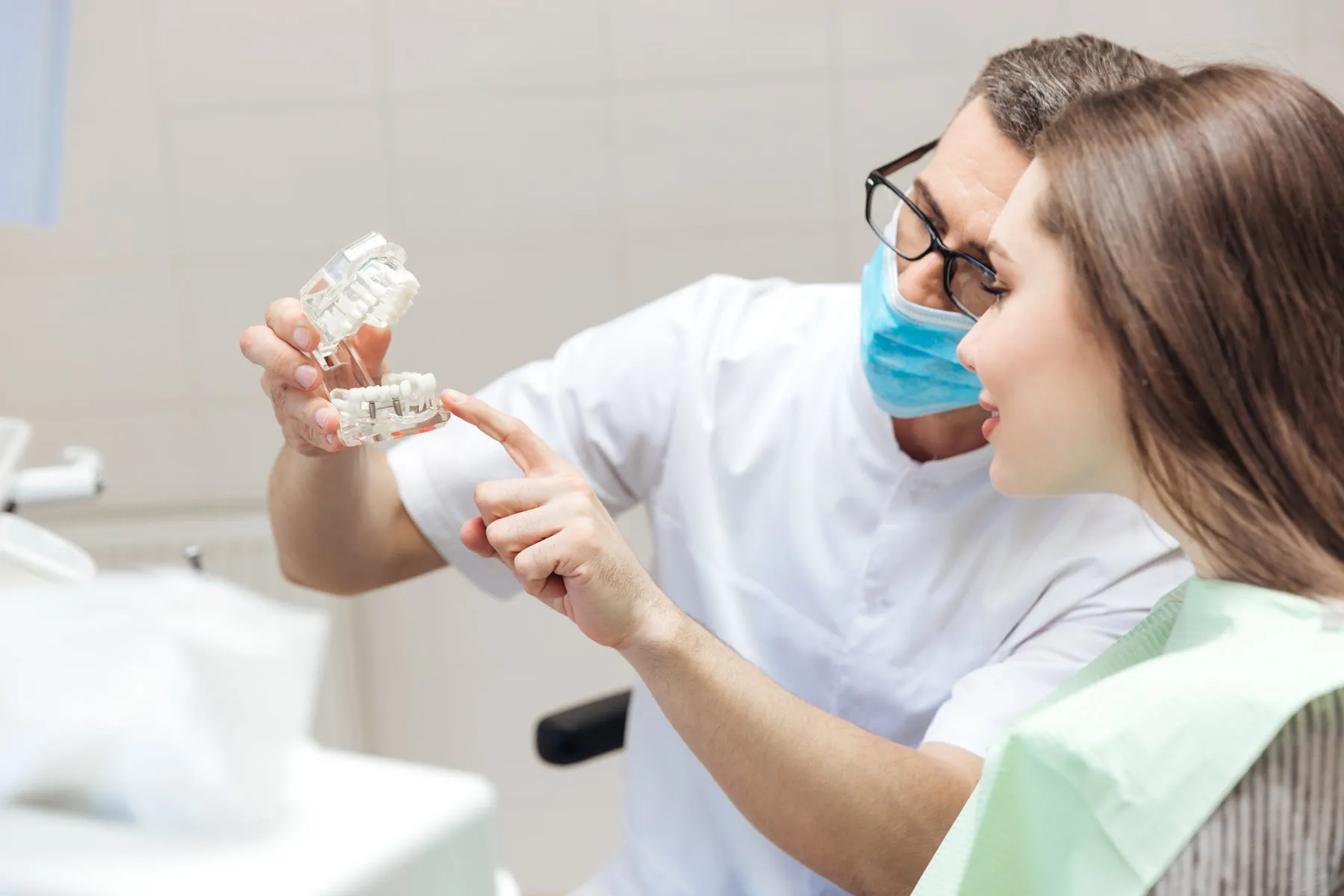 Couple smiling while looking at phone - Sunrise Dental Arts Care Man dentist show dentures teeth at dental surgery to patient