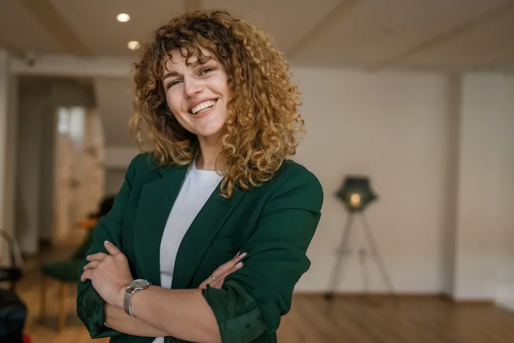 Confident woman with bright smile - Dentist in Bankers Hill A cheerful woman in a green blazer confidently smiling indoors, showing her healthy teeth - Dentist in Bankers Hill.
