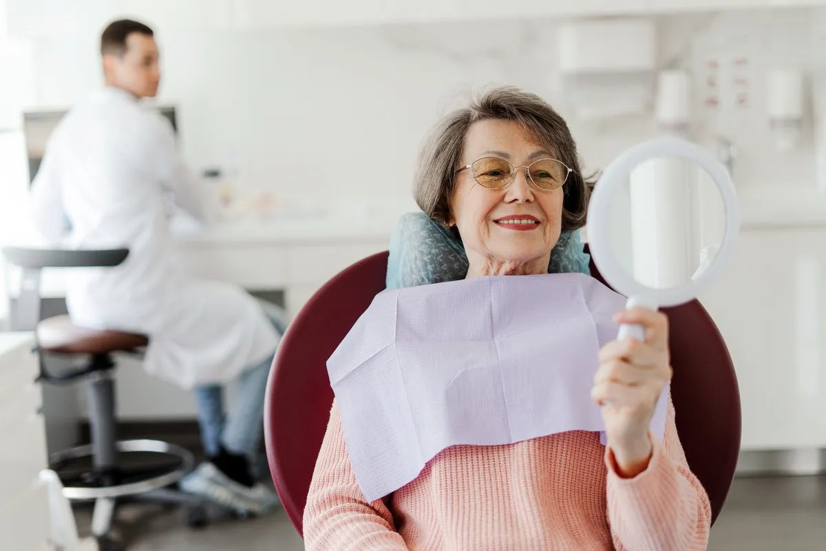 Couple smiling while looking at phone - Sunrise Dental Arts Care Patient, senior, mature woman holding mirror, looking, talking to senior professional dentist