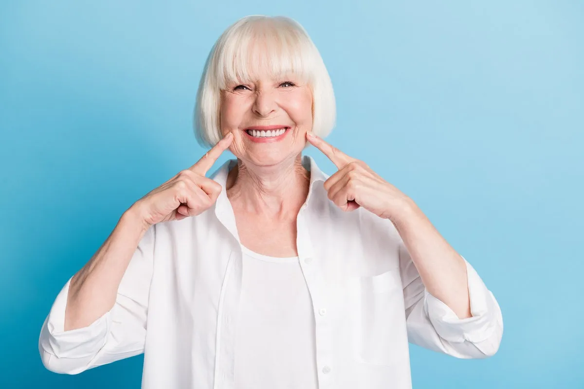 Happy couple smiling outdoors - Sunrise Dental Arts Care Photo portrait of granny blonde hair pointing at white teeth healthy smile dental whitening veneers isolated on bright blue color background