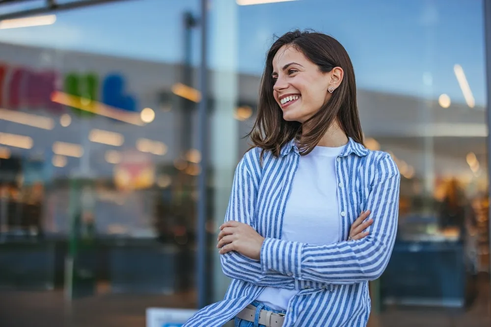 Woman smiling in striped shirt - North Park Dentist A happy woman in a blue and white striped shirt smiling brightly outdoors, showcasing her healthy teeth - North Park Dentist.