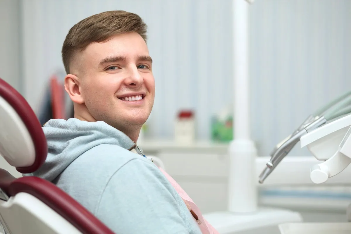 Couple smiling while looking at phone - Sunrise Dental Arts Care Portrait of happy satisfied smiling with white teeth young man patient with perfect smile, positive guy having a seat, sitting on dentist medical chair in dental office after treatment in clinic
