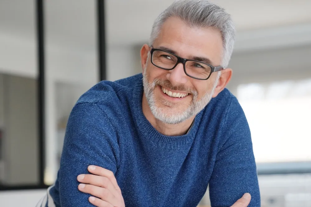 Mature man with confident smile - Dentist in Hillcrest A smiling middle-aged man with glasses and gray hair, radiating confidence and healthy teeth - Dentist in Hillcrest.
