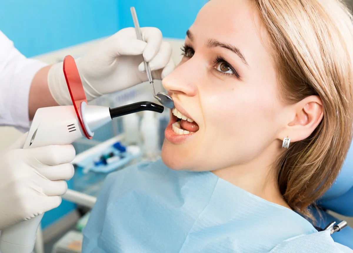 Couple smiling while looking at phone - Sunrise Dental Arts Care The reception was at the female dentist. Doctor examines the oral cavity on tooth decay. Caries protection. Tooth decay treatment. Dentist working with dental polymerization lamp in oral cavity