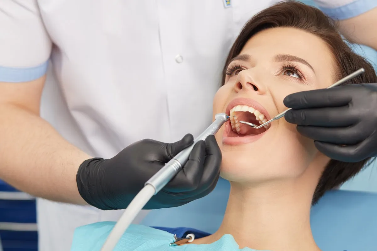 Man pointing at bright smile - Sunrise Dental Arts Care Young female patient visiting dentist office.Beautiful woman with healthy straight white teeth sitting at dental chair with open mouth during a dental procedure.Dental clinic.Stomatology.