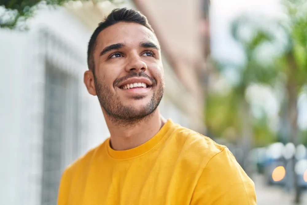 Smiling man in yellow shirt outdoors - North Park Dentist A cheerful young man in a yellow shirt smiling confidently outside, showing his bright teeth - North Park Dentist.