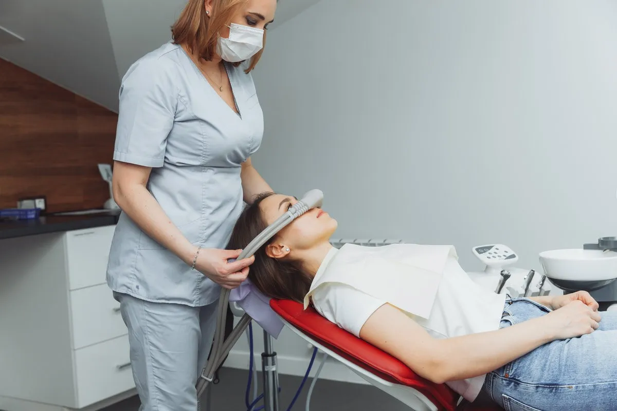Man pointing at bright smile - Sunrise Dental Arts Care dentist puts inhalation sedative mask on his adult patient.