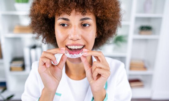 Woman smiling while holding a clear aligner tray