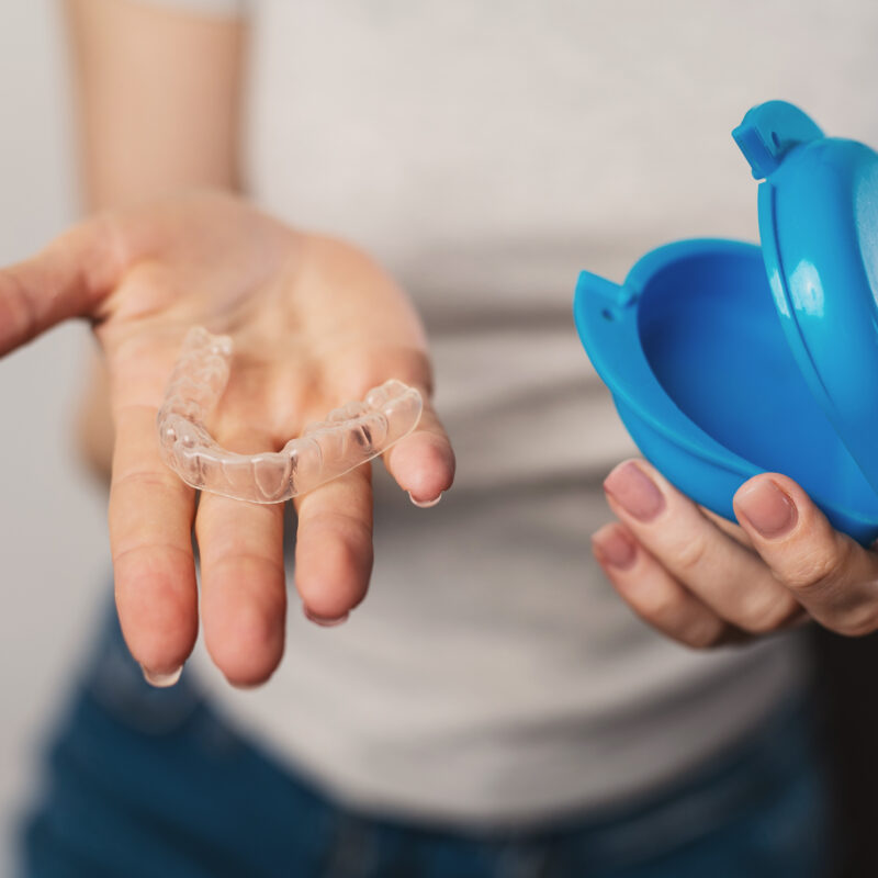 Woman holding a clear custom nightguard used to protect teeth from bruxism